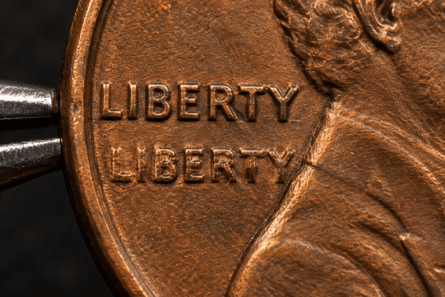 Macro close-up of a wheat cent's LIBERTY lettering showing a clear second ghost impression of each letter under raking light
