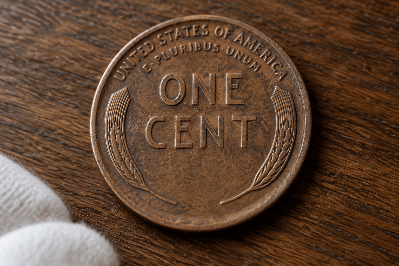 Reverse of a circulated Lincoln wheat cent showing two wheat stalks, ONE CENT, UNITED STATES OF AMERICA, and the E PLURIBUS UNUM motto arc under natural desk light